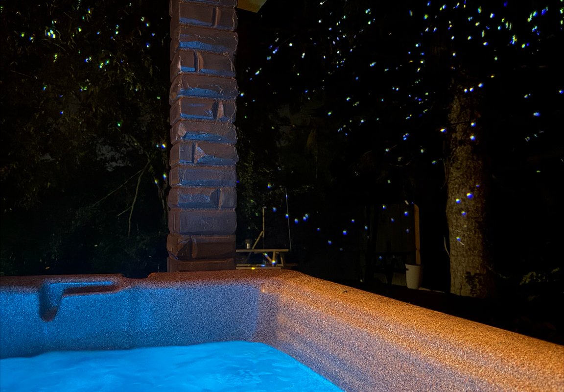 Private hot tub glowing at night under wooden pergola